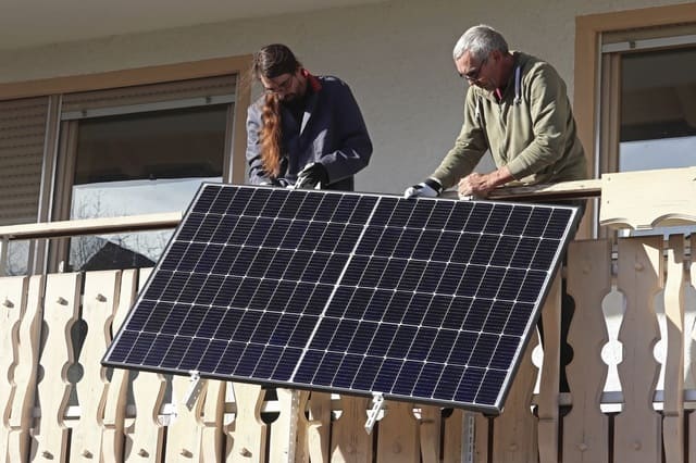 Balkonkraftwerk wird von zwei Personen installiert Photovoltaikanlage am Holzbalkon wird montiert